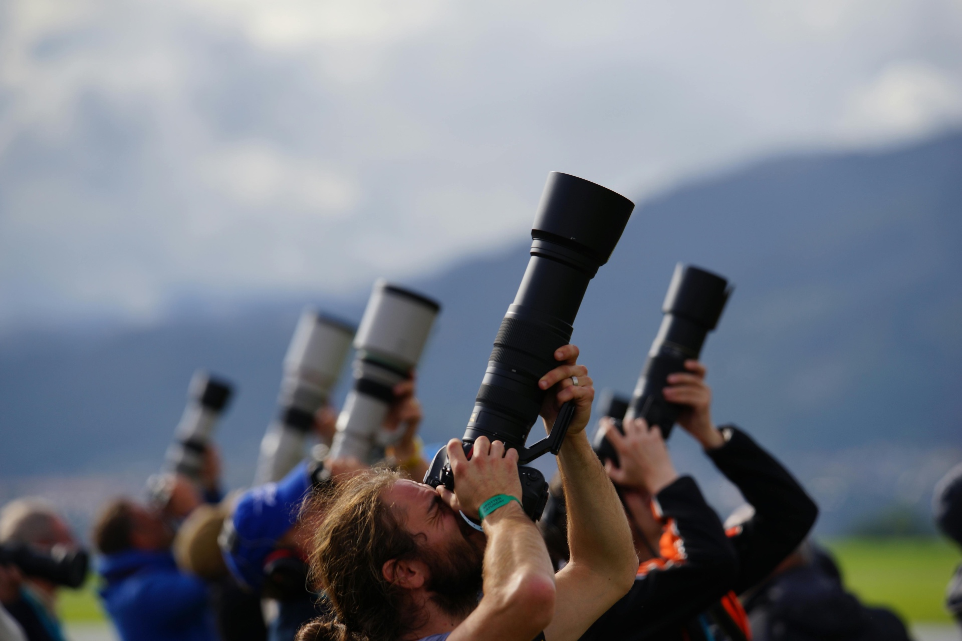 A row of photographers with telephoto lenses pointed skyward against a mountain backdrop.